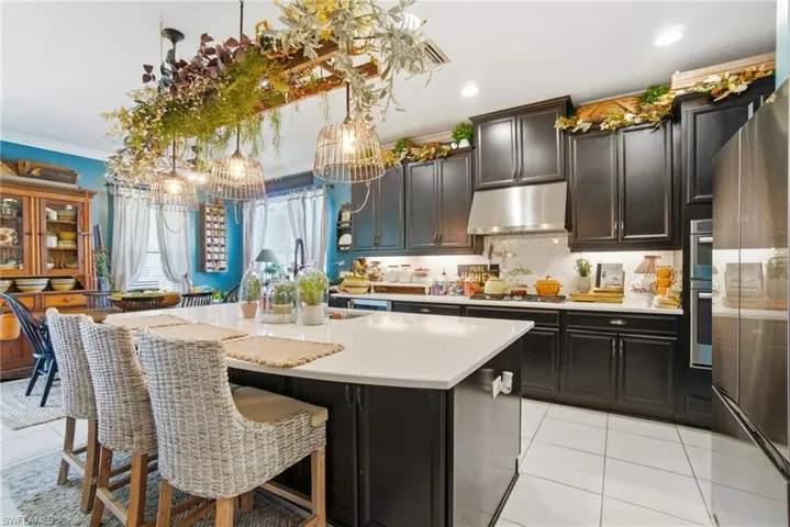 Kitchen featuring ornamental molding, light tile patterned floors, backsplash, a kitchen breakfast bar, and appliances with stainless steel finishes