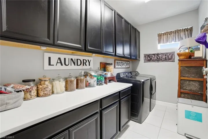 Laundry area with light tile patterned floors, washer and clothes dryer, and cabinet space