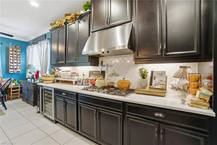 Kitchen with under cabinet range hood, light tile patterned floors, backsplash, beverage cooler, and stainless steel gas stovetop