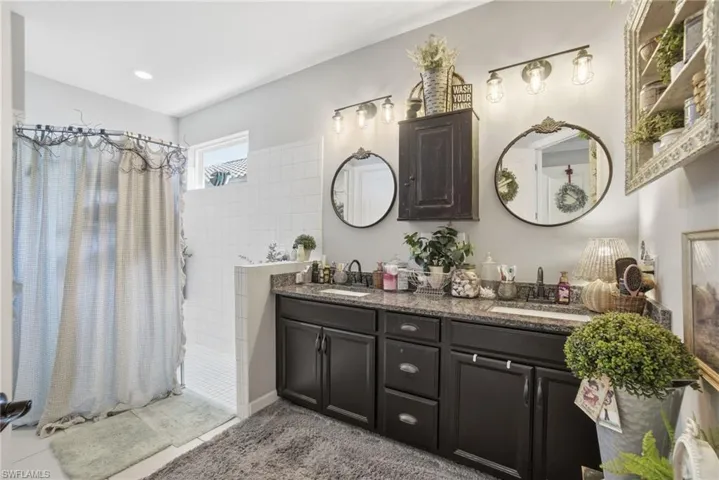 Bathroom with double vanity, tiled shower, and light tile patterned flooring