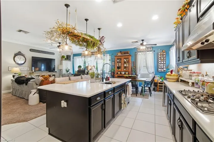 Kitchen featuring open floor plan, crown molding, under cabinet range hood, stainless steel gas cooktop, and light tile patterned floors