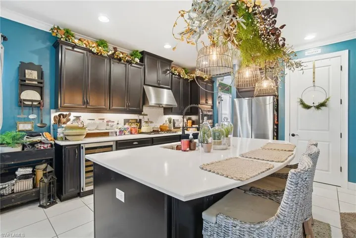 Kitchen with light tile patterned floors, ornamental molding, a breakfast bar, beverage cooler, and a center island with sink