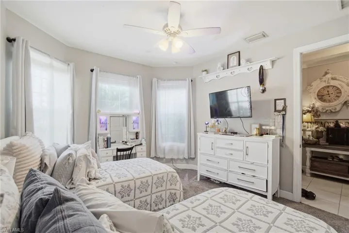 Bedroom with multiple windows, ceiling fan, light carpet, and light tile patterned floors