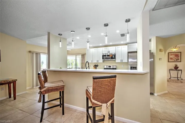 Kitchen featuring stainless steel appliances, white cabinets, pendant lighting, light tile patterned floors, and a textured ceiling