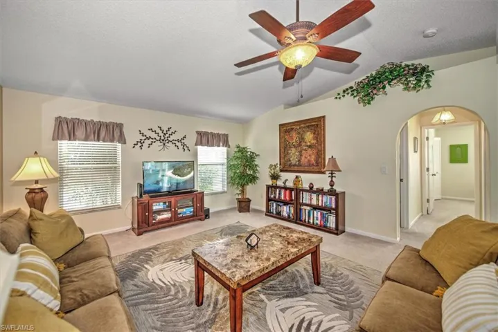 Living room with a textured ceiling, ceiling fan, lofted ceiling, and light colored carpet