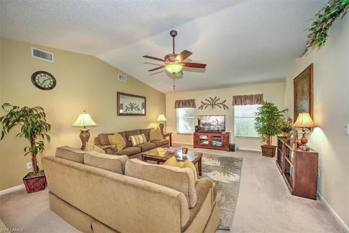 Carpeted living room featuring lofted ceiling, a textured ceiling, and ceiling fan
