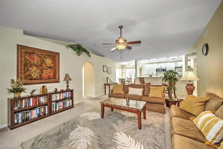 Living room featuring a textured ceiling, vaulted ceiling, light colored carpet, and ceiling fan