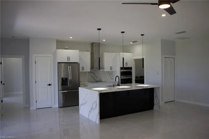 Two tone kitchen with stainless steel appliances, light stone countertops, a kitchen island with sink, pendant lighting, and tasteful backsplash