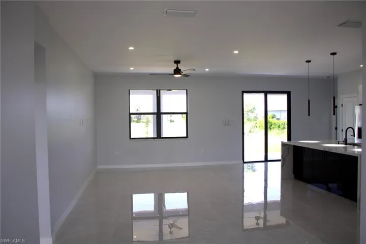 Kitchen featuring a ceiling fan, hanging light fixtures, light stone countertops, open floor plan, and an island with sink