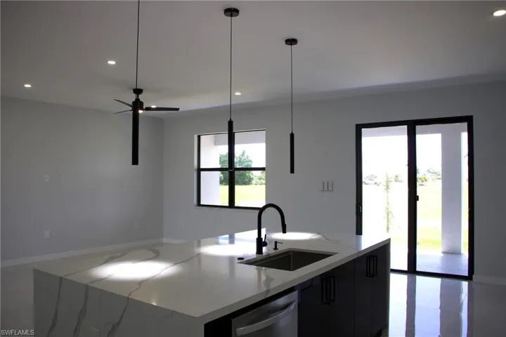 Kitchen with light stone counters, an island with sink, modern cabinets, stainless steel dishwasher, and a ceiling fan