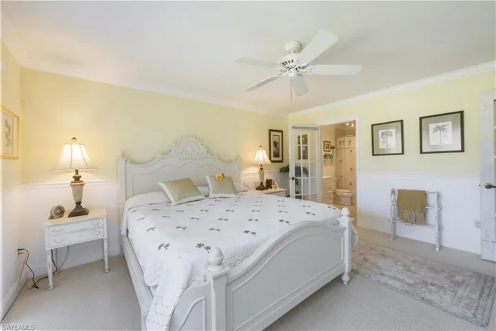 Carpeted bedroom with a wainscoted wall, ornamental molding, a ceiling fan, and connected bathroom