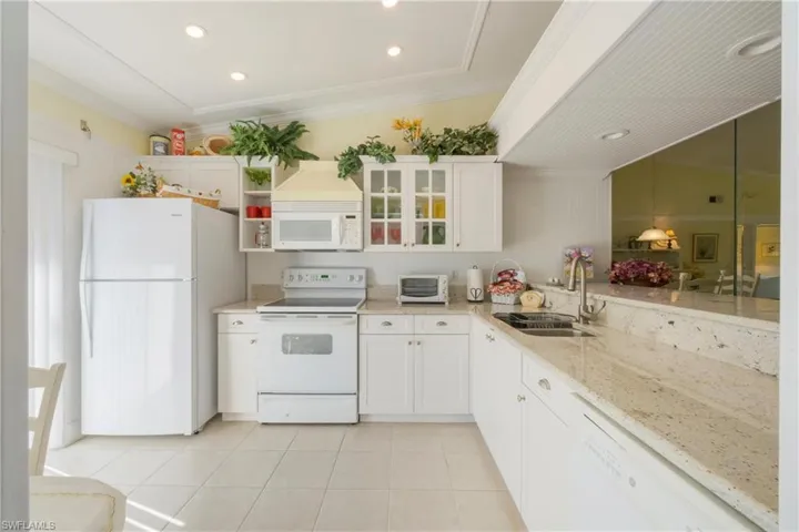 Kitchen with white cabinetry, white appliances, ornamental molding, light stone countertops, and recessed lighting