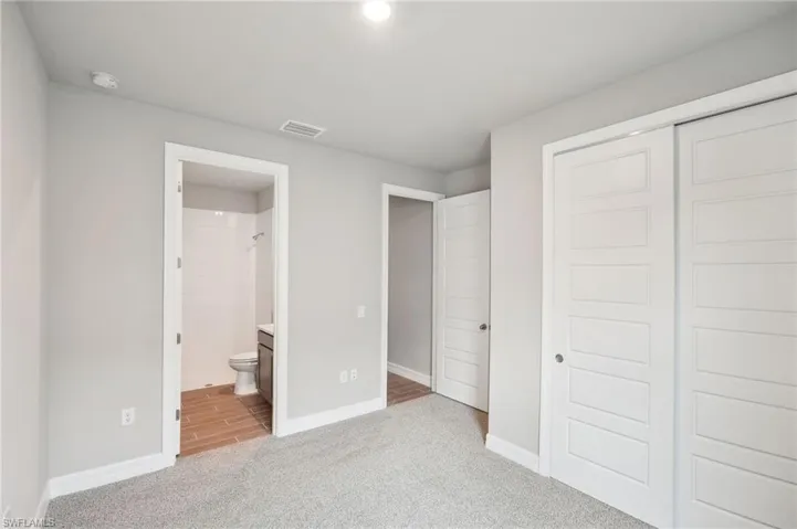 Unfurnished bedroom with a closet, light carpet, and connected bathroom