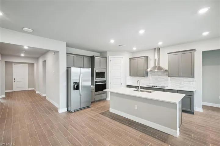Kitchen featuring wall chimney exhaust hood, sink, a kitchen island with sink, light wood-type flooring, and appliances with stainless steel finishes