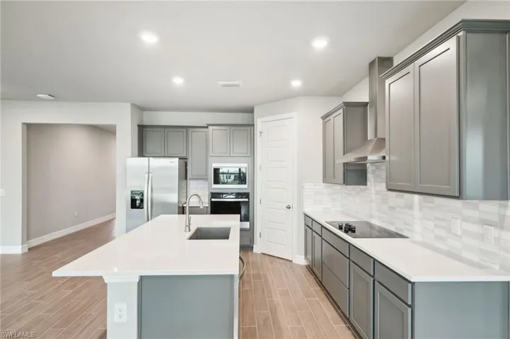 Kitchen with a center island with sink, gray cabinetry, sink, and black appliances