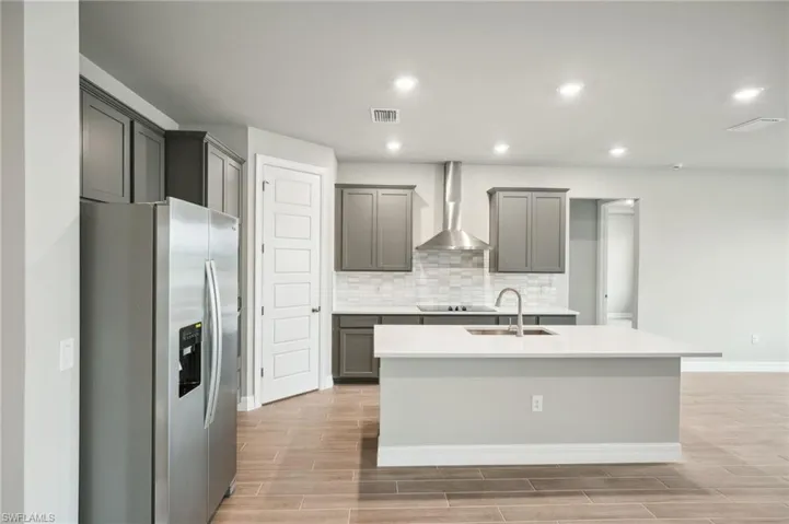 Kitchen with wall chimney exhaust hood, sink, stainless steel fridge with ice dispenser, a kitchen island with sink, and light wood-type flooring