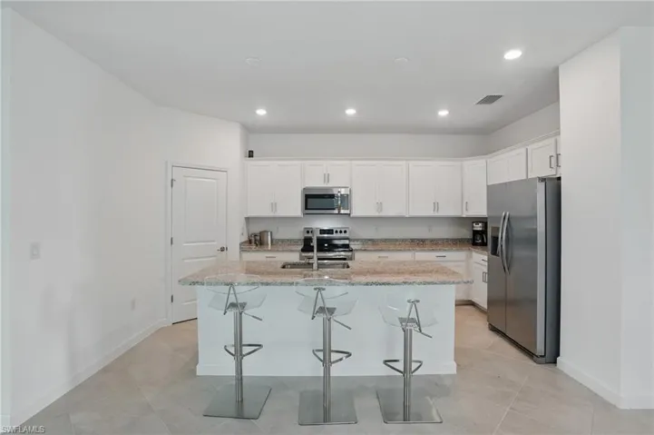 Kitchen featuring stainless steel appliances, a center island with sink, white cabinetry, baseboards, and recessed lighting
