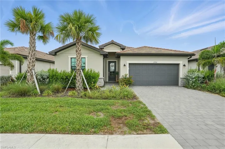 Single story home featuring an attached garage, stucco siding, decorative driveway, and a front yard