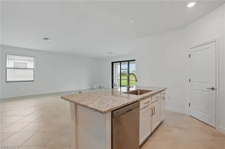 Kitchen featuring stainless steel dishwasher, a sink, open floor plan, an island with sink, and light tile patterned floors