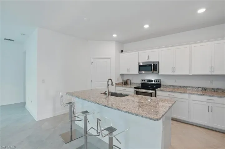 Kitchen with stainless steel appliances, a sink, a kitchen island with sink, white cabinetry, and light stone countertops