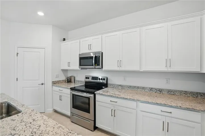 Kitchen with stainless steel appliances, white cabinets, light tile patterned floors, light stone counters, and recessed lighting