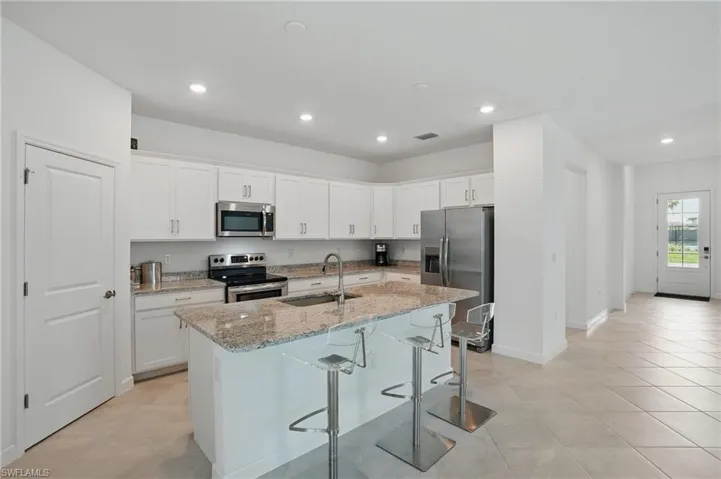 Kitchen featuring stainless steel appliances, a sink, an island with sink, light stone countertops, and a kitchen breakfast bar
