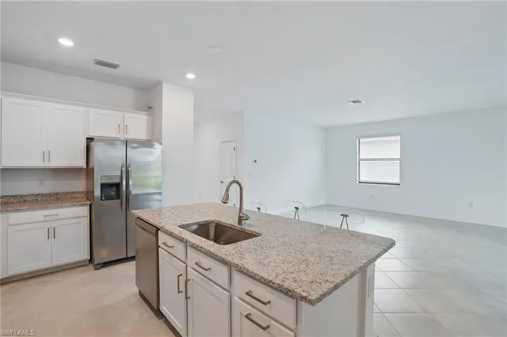 Kitchen featuring stainless steel appliances, a sink, white cabinets, light tile patterned floors, and a kitchen island with sink