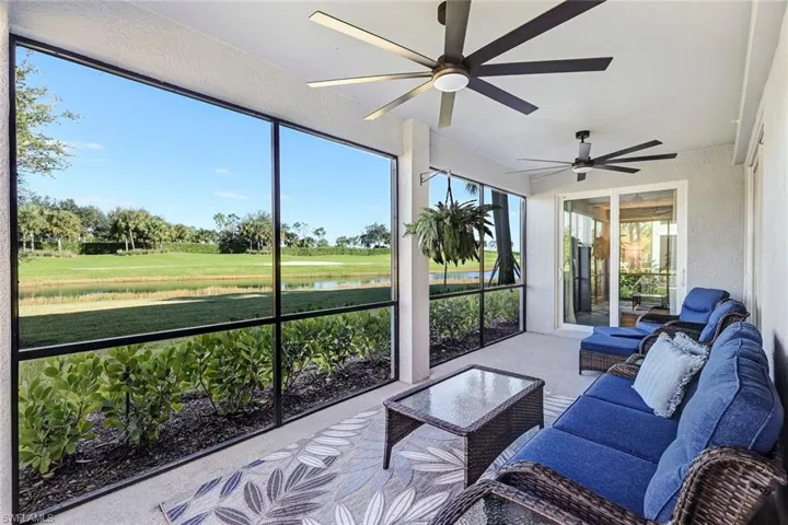 Screened-in lanai featuring concrete flooring, dual ceiling fans, and large-format glass window panels overlooking the golf course, landscaped lawn and pond