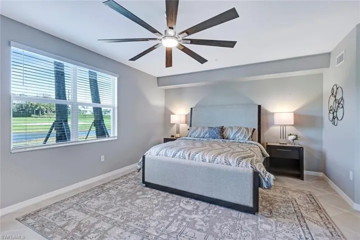 Neutral-toned interior featuring oversized tile flooring, a multi-blade ceiling fan with integrated lighting, and large windows with horizontal blinds and golf course view