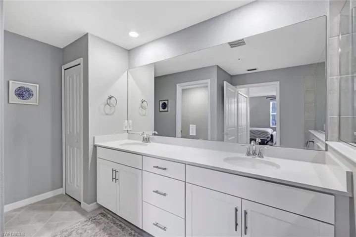 Dual-sink vanity with a solid-surface countertop, white shaker-style cabinetry, chrome fixtures, and a large-format vanity mirror