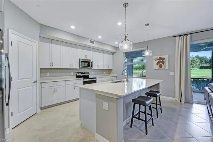 Kitchen featuring shaker-style white cabinetry, quartz countertops, a central island with a double basin sink, and globe pendant lighting