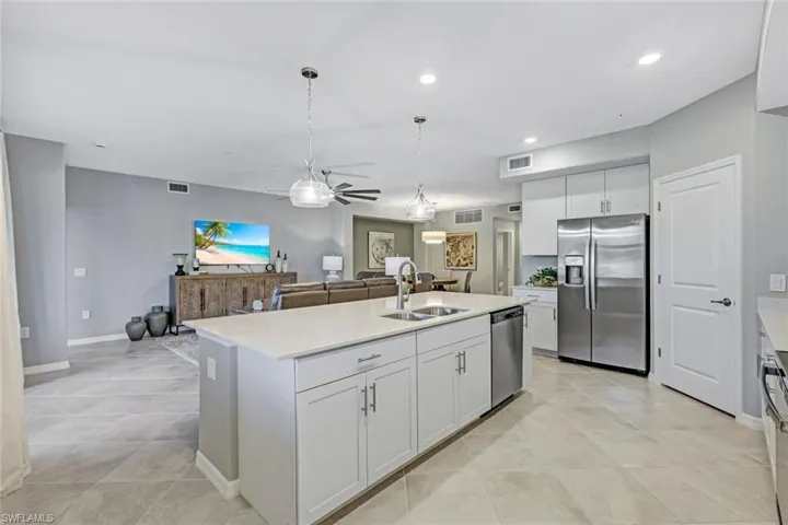 Kitchen featuring a central island with a solid quartz countertop, stainless steel refrigerator and dishwasher, white cabinetry, and large-format tile flooring