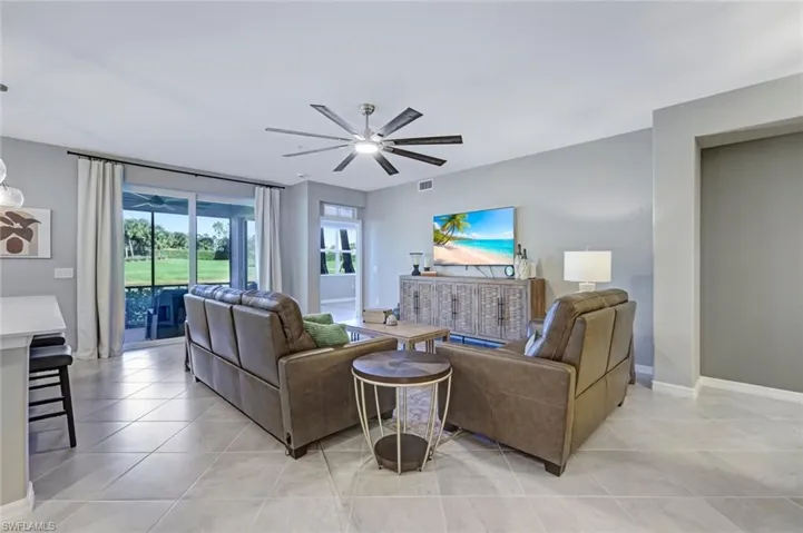 Large-format tile flooring, multi-blade ceiling fan, and expansive hurricane impact sliding glass doors providing outdoor access