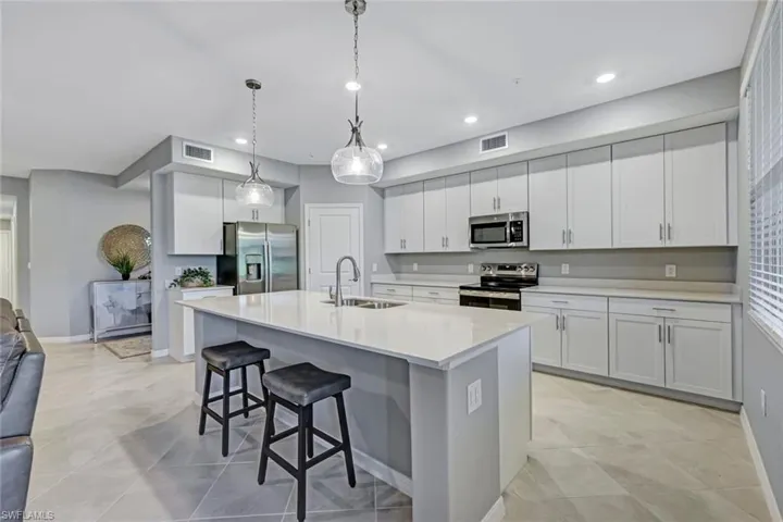 Kitchen featuring white shaker-style cabinetry, quartz countertops, a central island with a double-basin undermount sink, stainless steel appliances, and pendant lighting