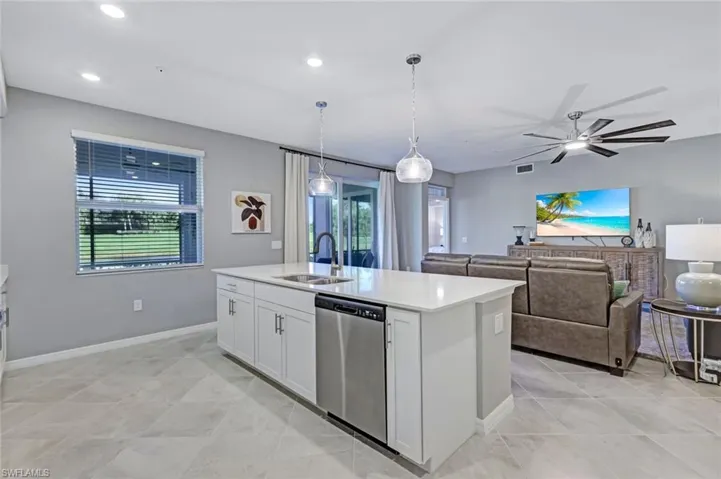 Kitchen island featuring a quartz countertop, under-mount stainless steel sink, and stainless-steel dishwasher, complemented by tile flooring and dual pendant lighting