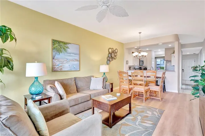 Living room featuring ceiling fan with notable chandelier and wood-type flooring
