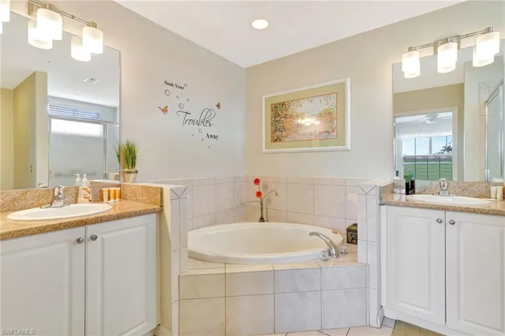 Bathroom with tile flooring, tiled tub, and double sink vanity