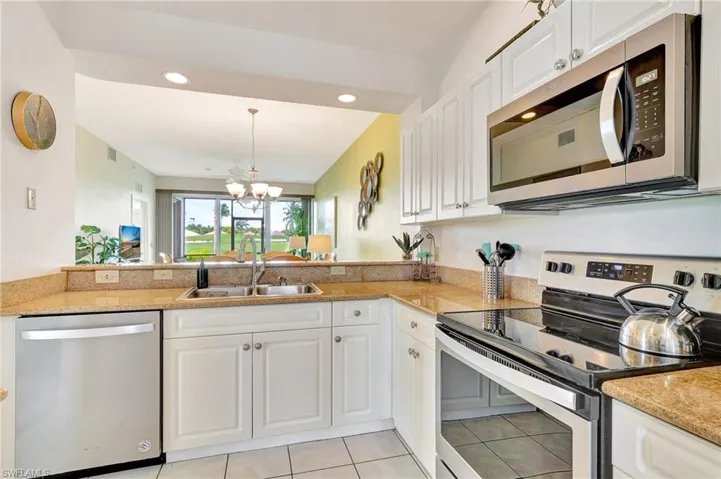 Kitchen with light stone counters, white cabinets, sink, light tile floors, and appliances with stainless steel finishes