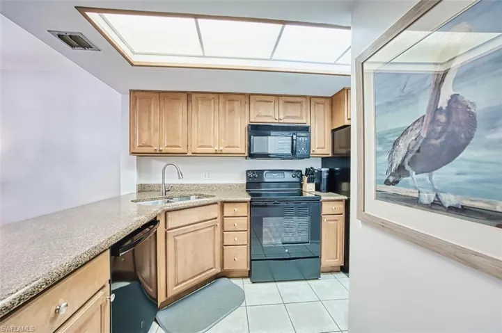 Kitchen featuring black appliances, a sink, light tile patterned floors, light stone counters, and light brown cabinets