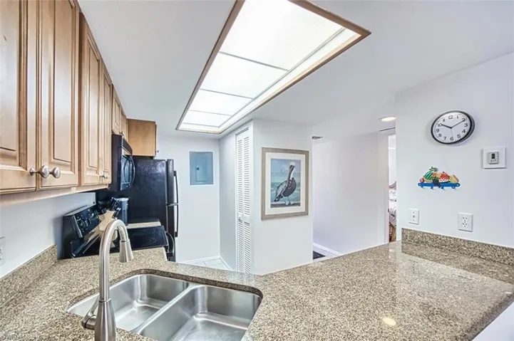 Kitchen featuring stainless steel electric range oven, a sink, brown cabinetry, light stone countertops, and a peninsula