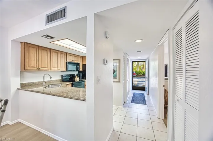Kitchen featuring black appliances, a sink, stone countertops, baseboards, and light tile patterned floors