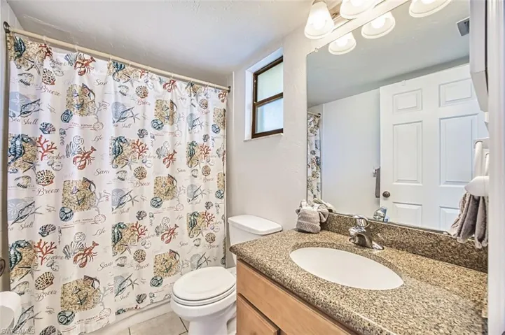 Full bath with toilet, vanity, tile patterned floors, and curtained shower
