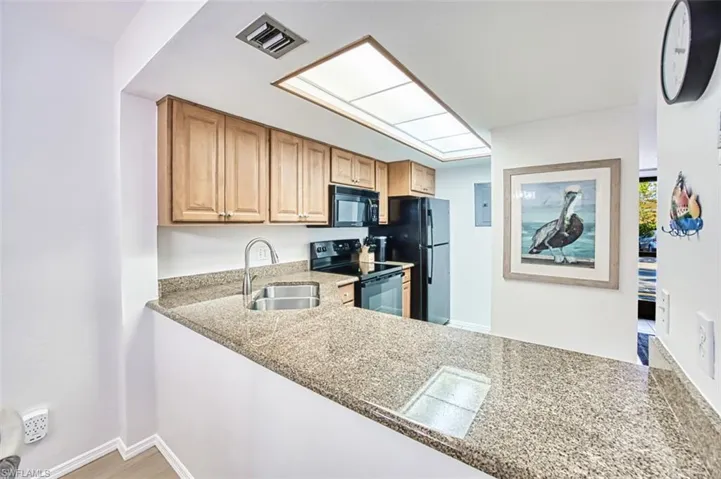 Kitchen featuring black appliances, a sink, electric panel, and baseboards