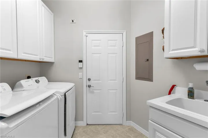 Laundry room with cabinet space, washing machine and dryer, light tile patterned flooring, electric panel, and baseboards