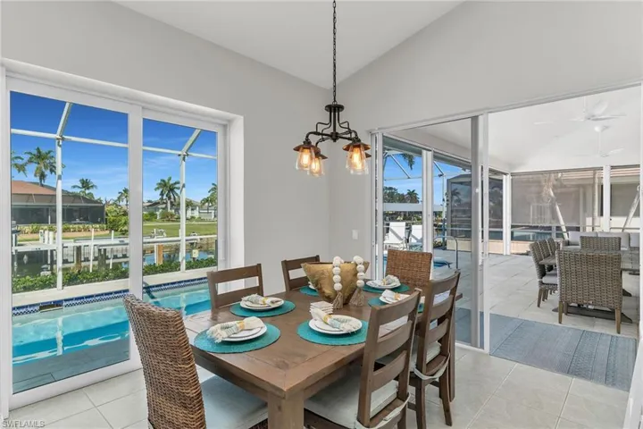Dining space with lofted ceiling, light tile patterned floors, and ceiling fan with notable chandelier