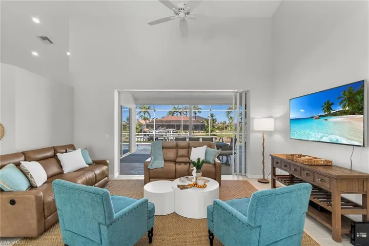 Living area with visible vents, a towering ceiling, a ceiling fan, a sunroom, and baseboards