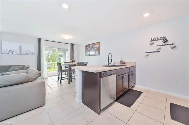 Kitchen featuring dishwasher, open floor plan, light countertops, light tile patterned floors, and dark brown cabinets