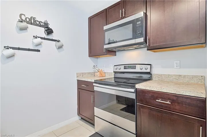Kitchen with stainless steel appliances, dark brown cabinetry, light countertops, and light tile patterned floors