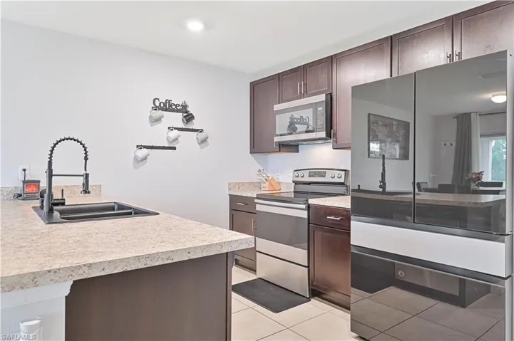 Kitchen featuring stainless steel appliances, dark brown cabinetry, light tile patterned floors, light countertops, and recessed lighting