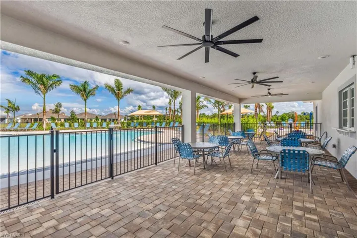 Covered patio featuring multiple ceiling fans, paver flooring, and direct access to a swimming pool with a black iron fence